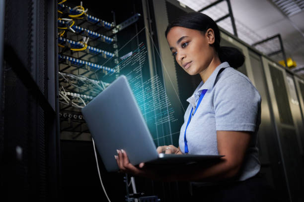 istock Laptop, network and data center with a black woman it support engineer working in a dark server room. Computer, cybersecurity and analytics with a female programmer problem solving or troubleshooting 1633491908