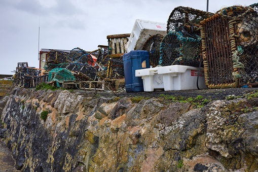 St Abbs, Berwickshire, Scotland, Uk. 28th March 2023. A pile of lobster traps and plastic boxes line the harbour wall at St Abbs