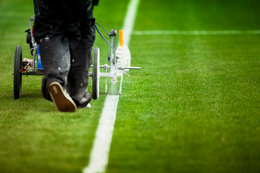 Stadium green playing surface for soccer and football being spray painted by the maintenance grounds crew before a match or game