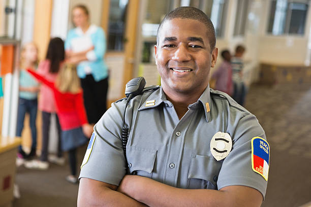 sonriente agente de policía que proporciona seguridad en la escuela campus - arms crossed audio fotografías e imágenes de stock