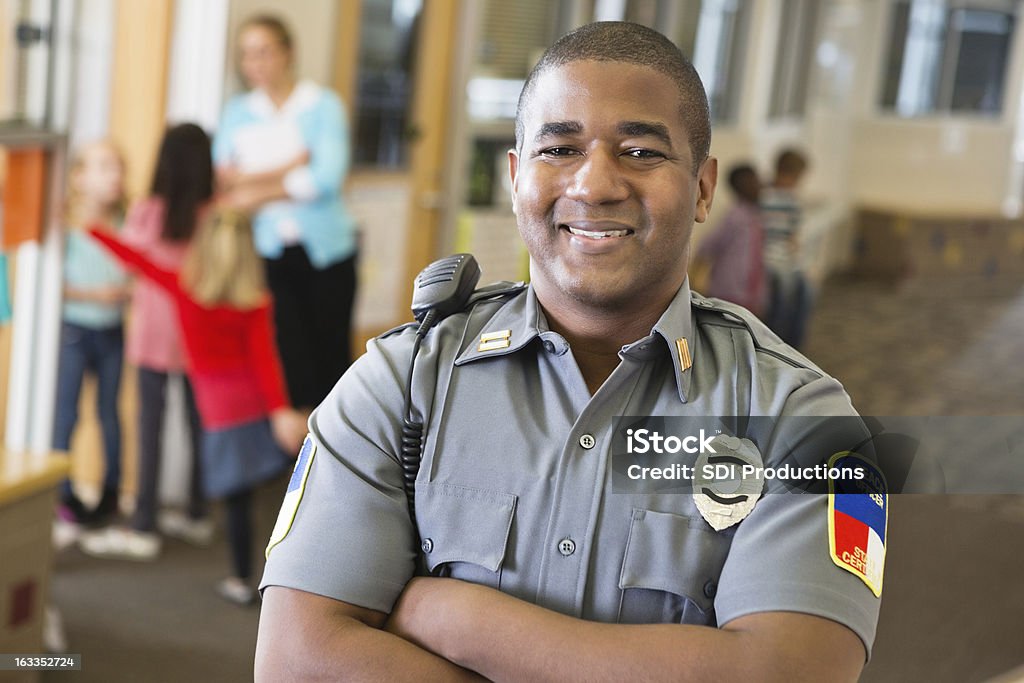 Sorridente amichevole agente di polizia che garantiscono la sicurezza su campus scolastici - Foto stock royalty-free di Forze di polizia