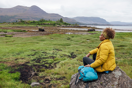 A wide angle view of a mature woman who is grounding herself and taking a moment to appreciate the beauty in nature and the stunning landscape in Loch Torridon in the Scottish Highlands.