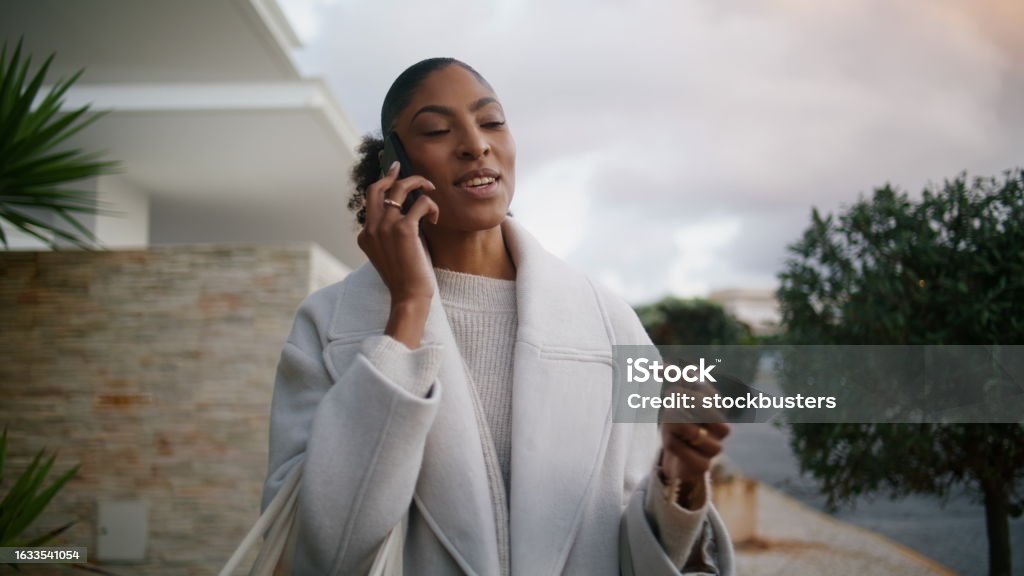 Attractive african american talking phone on street. Wealthy rich woman walking Attractive african american talking phone on street. Wealthy rich woman walking city hold key in hand. Stylish smiling businesswoman consult client partner after work. Successful real estate manager. Adult Stock Photo