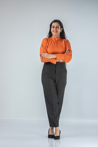 Portrait of smiling Indian businesswoman dressed in formalwear with arms crossed standing confidently against white background