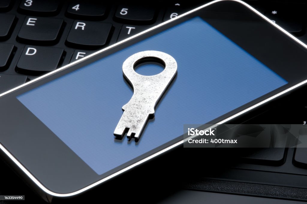 Digital Cell Phone Security Concept Antique key lying on a cell phone with a keyboard background. Blue Stock Photo