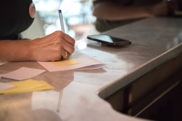 istock Woman's hand holding a pen and writing a message on a paper. Smart phone resting on the table or counter. Contrast between handwriting and new technologies. Close up. 1633551873