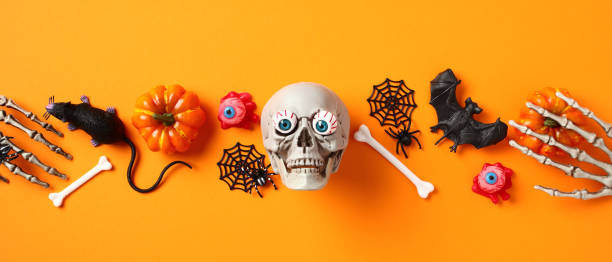 istock Happy Halloween banner. Top view skull, bones, bats, spiders, pumpkins with skeleton hands on orange background. 1633551881