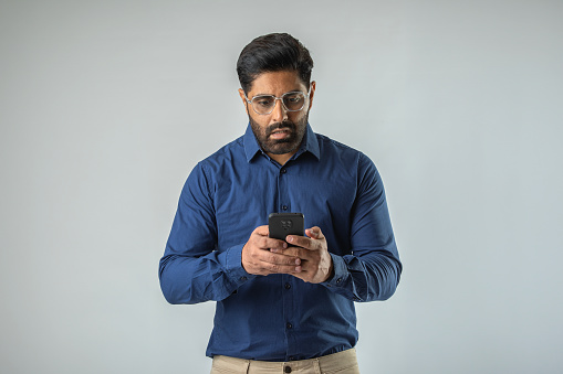 Shocked mid adult businessman reading message over smart phone while standing against white background
