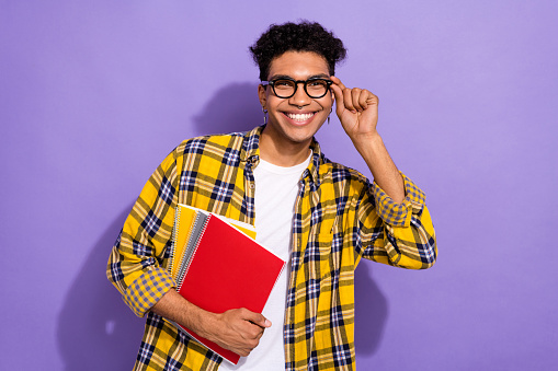 Photo of positive cheerful guy wear plaid yellow shirt arm spectacles holding copybooks isolated violet color background.
