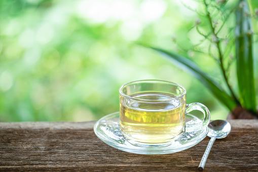 A cup of green tea on wooden table with leaf and natural background, beverage for relaxation.