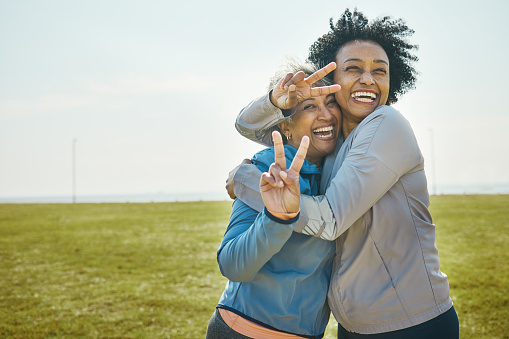 Senior, women hug and fitness, peace hand sign and portrait with friends, energy and playful outdoor. Happy female people, friendship and cool with sportswear in park, exercise and fun together