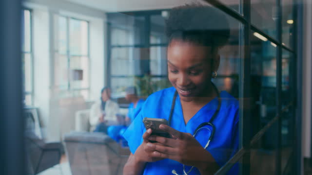 Close up of female millennial nurse dressed in scrubs using smartphone to send text messages indoors hospital. Happy young  doctor texting with cell phone inside clinic.