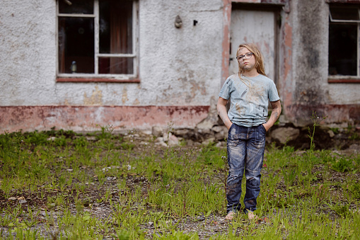 Dirty 'trailer trash' 8-year-old standing guard in front of her derelict home. Posed by model.
