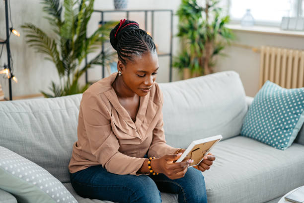 istock Young Woman Holding A Picture Frame While Sitting On The Sofa At Home 1633639523