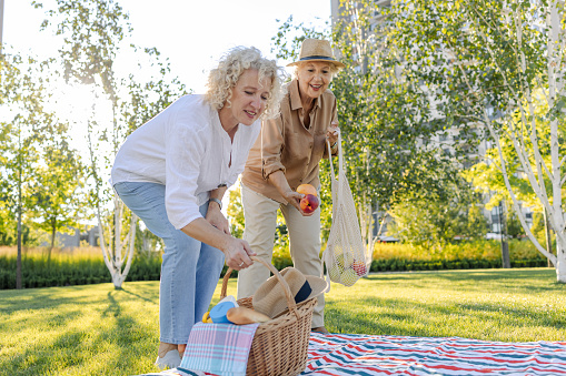 Mature and senior woman are enjoying outdoors. They are preparing a picnic in a park.