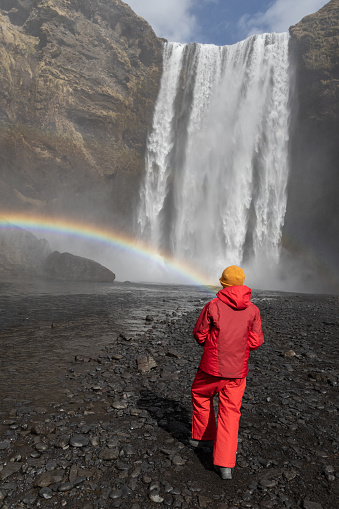Skogafoss waterfall Iceland, rainbow in front of a girl in a red jacket