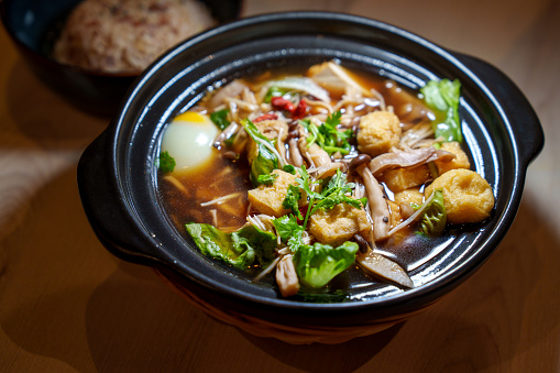 A claypot of vegetarian herbal soup is shown, featuring fried bean curd, various types of mushrooms, and leafy vegetables. This dish is a delightful example of vegetarian cuisine.