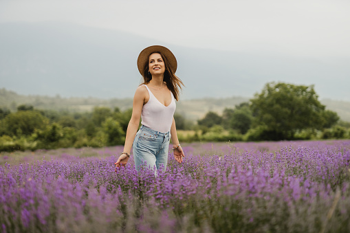 A beautiful young woman with a hat walking through the lavender field on a lovely day outside