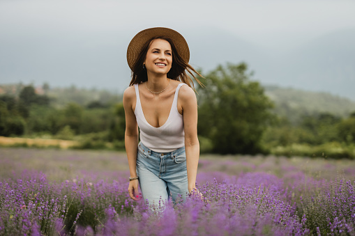 Portrait of a beautiful young casually dressed woman with a hat enjoying a lovely summer day in the lavender field