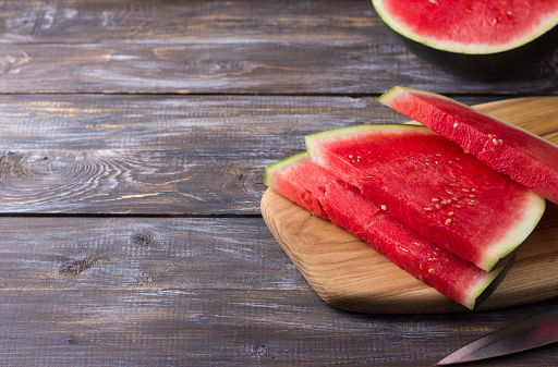Seedless watermelon, slices on a wooden board with a knife and half of a watermelon on a wooden background, copy space.
