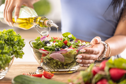 The final preparation of a healthy salad and at the end the woman pours olive oil.