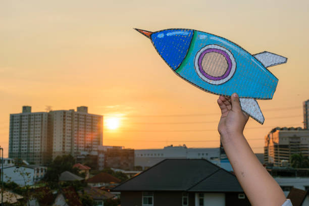 istock Child hands holding rocket, standing on skyscraper, art in backlight, holding hands launching spaceship on blurred city background. 1633753444