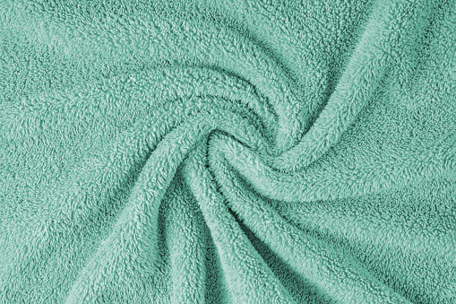 Terry cloth, turquoise towel texture background. Wrinkled and crumped soft fluffy textile bath or beach towel material. Top view, close up.