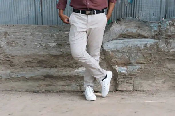 Man standing on the floor with cream pants and white canvas shoes. Cream color with white sneakers for men. MUJI fashion for men with cement wall.