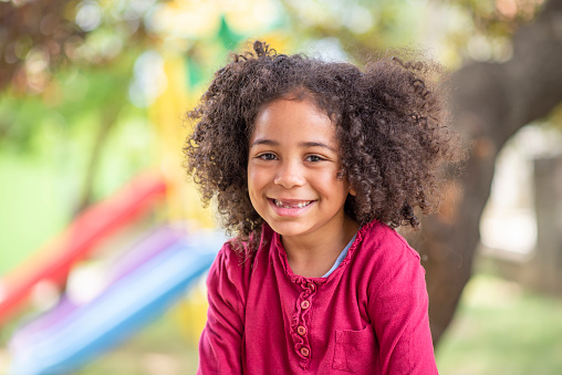 Smiling cute little African American girl with curly hair looking at camera. Portrait of happy African American girl playing in the park.