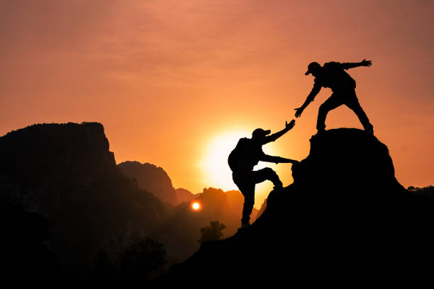 istock Amidst the echoing rays of sunlight, the mountain climber is extending a helping hand to pull their friend up to the mountaintop summit. 1633798140