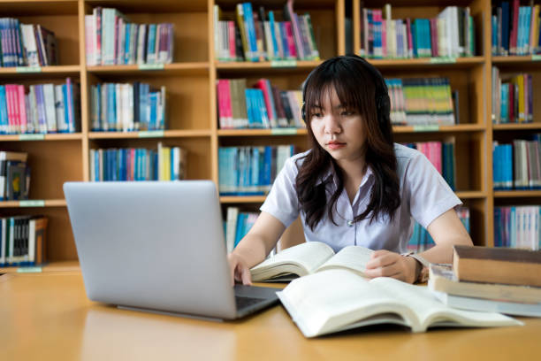 istock Young Asian female university student concentrate on studying, doing assuagement project in library with books and laptop on table 1633819165