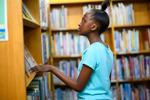 Young African girl looking at all the library books on the shelves