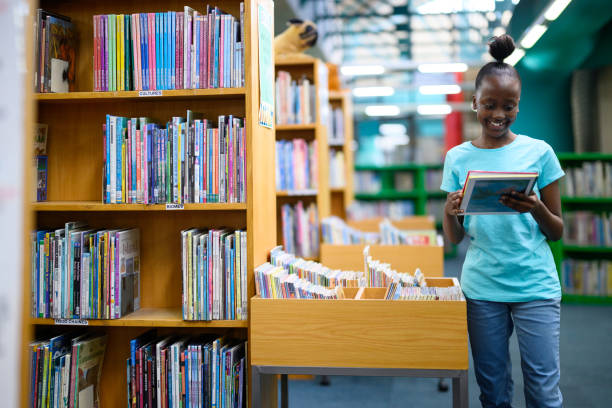 istock Smiling girl standing in library holding a storybook 1633829072