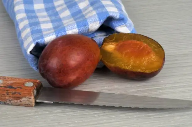 Whole plum and half plum with a knife close-up