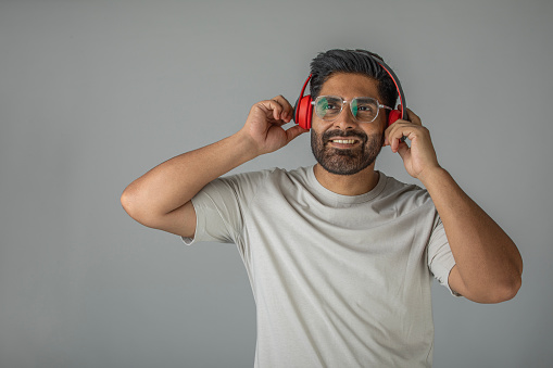 Cool handsome mid adult man listening music over headphones and looking away against white background