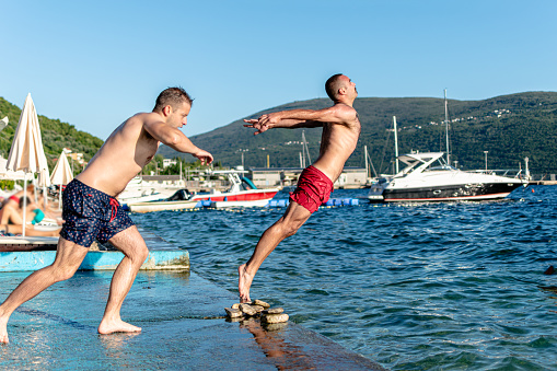 This image captures a beachside moment as two friends embrace the sea by jumping into the water for a refreshing dip