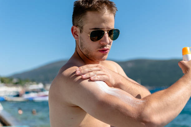 istock Young man conscientiously applies sun protection on the beach 1633842794
