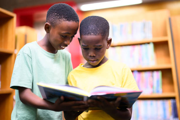 istock Close up two boys standing looking through book together 1633844516