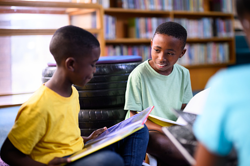 Group of happy young boys sitting on the floor in the library reading story books