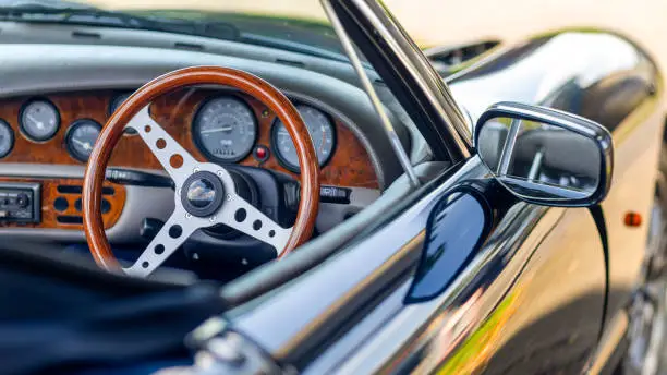Photo of Beautiful wooden steering wheel and and old-fashioned small gauges and large beautiful exterior mirror of a historic cabriolet - right-hand drive