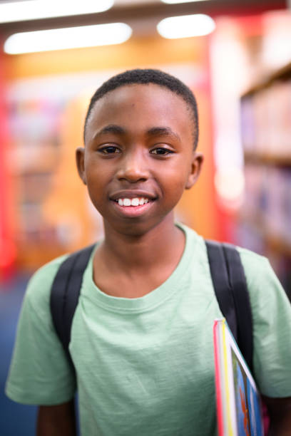 istock Close up portrait boy holding a book in library with backpack 1633854262