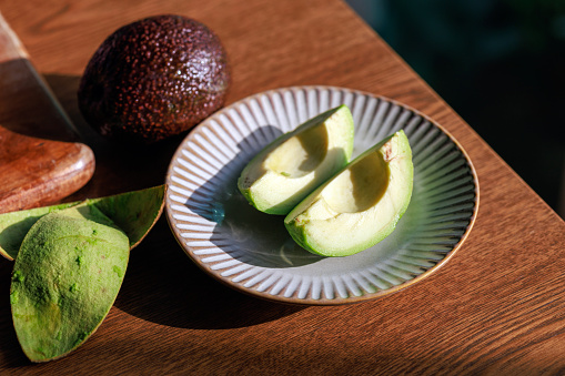 Slices of fresh avocado arranged on a wooden cutting board, illuminated by the morning sunlight.