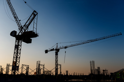 Silhouettes of two tower cranes on the construction site.