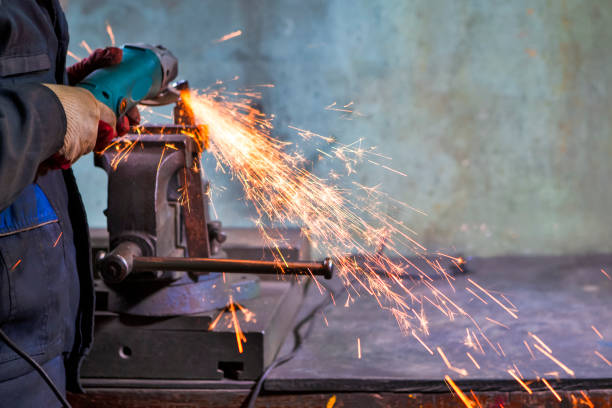 Metal Processing Concepts. One Man Fitter in Protective Gloves and Uniform With Gringer Tool For Metal Work With Bunch of Sparks in Workshop