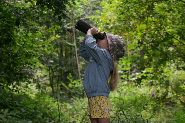 Cute little girl exploring nature looking through binoculars. Child playing outdoors. Kids travel, adventure and bird watching concept.