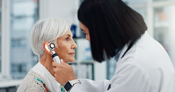 Senior woman, doctor and otoscope for ear, hearing test and exam, audio check or consultation for healthcare. Ent, otolaryngology and medical professional with elderly person for wellness in hospital