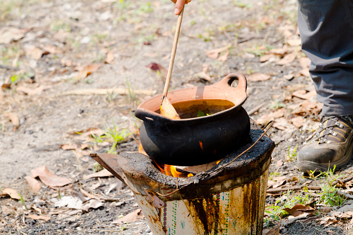 Thai man is stirring food in clay pot on fireplace in Chiang Mai province