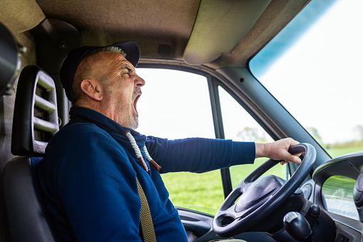 Mature truck diver feeling tired and yawning during the ride.