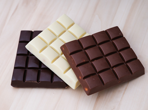 Three chocolate bars - milk chocolate, dark chocolate and white chocolate on a wooden background.
