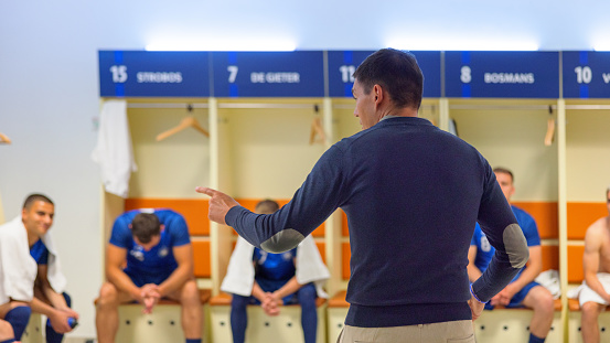 Coach explaining game strategy to football players in dressing room.